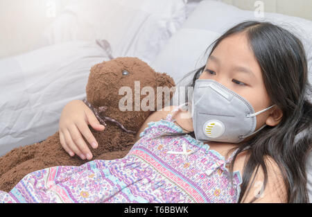 Asian girl portant un masque anti-poussières PM2,5 sur lit, concept de soins de santé Banque D'Images