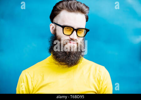 Close-up portrait of a confondu barbu dans chandail jaune et des lunettes de soleil sur le fond bleu Banque D'Images