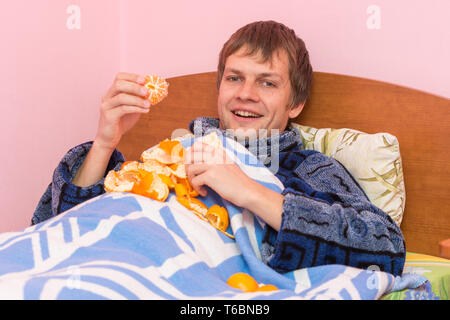 Heureux jeune homme mange des mandarines au lit Banque D'Images