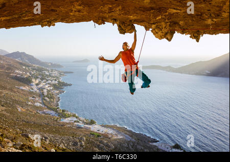 Male rock climber sur route difficile en longeant le plafond en cave, Kalymnos, Grèce Banque D'Images