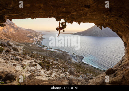 Jeune femme escalade dans la grotte au coucher du soleil, l'île de Kalymnos, Grèce Banque D'Images