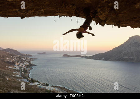 Female rock climber hanging upside down sur route difficile dans la grotte au coucher du soleil, se reposer avant sa tentative de maintien Banque D'Images