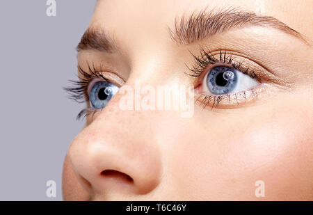 Closeup macro portrait de visage de femme. Femme humaine ouvrir les yeux bleus avec beauty maquillage de jour. Fille avec une peau parfaite et des taches de rousseur. Banque D'Images