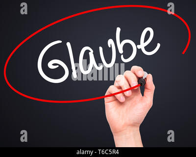 Man main écrit Glaube (Croyez en allemand) avec marqueur noir sur l'écran visuel. Banque D'Images