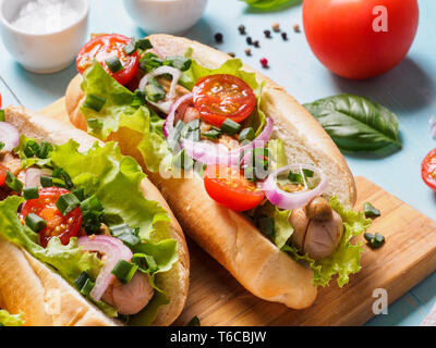Vue de près des hot-dogs avec des saucisses de poulet, légumes frais sur fond de bois bleu. Hot-dogs avec tomates, oignons, basilic, letucce et épices. Banque D'Images