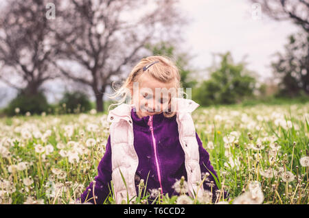 Adorable petite fille blonde s'amusant en champ de pissenlit printemps Banque D'Images