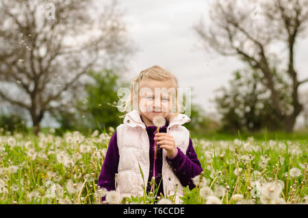 Adorable blonde girl blowing dandelion flower in belle prairie Banque D'Images