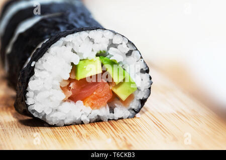 Des sushis au saumon, avocat, riz aux algues et baguettes sur la table en bois Banque D'Images
