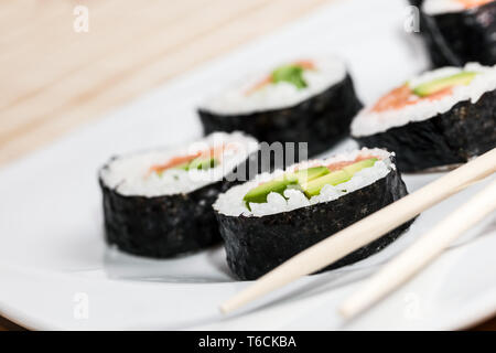 Des sushis au saumon, avocat, riz aux algues et baguettes sur une plaque. Banque D'Images