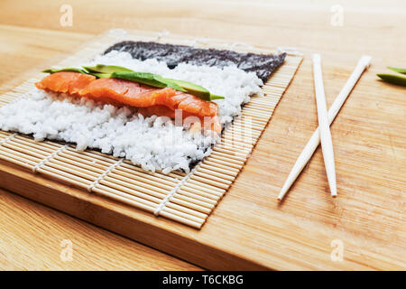 La préparation des sushis. Le saumon, avocat, riz et baguettes sur la table en bois. Banque D'Images