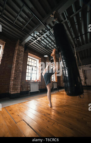 Un homme athlétique formation avec un sac de boxe dans la salle de sport. Le sac avec un coup de jambe Banque D'Images