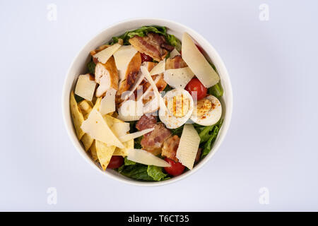 Salade César classique mise au point sélective avec poivrons grillé, bacon, œufs de caille, feuilles de laitue, chips, parmesan, tomates cerise sur le rond blanc pla Banque D'Images