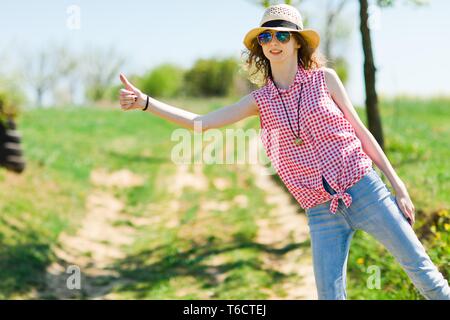 Jeune fille avec chapeau contre l'auto-stop sur la route de - chaude journée d'été dans la nature Banque D'Images