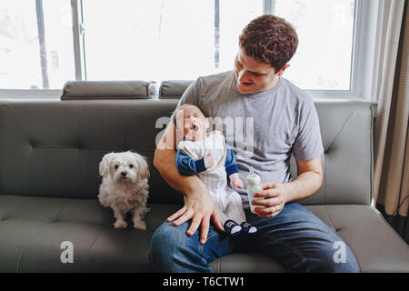 Young Caucasian père allaitement nouveau-né avec du lait. Mâle homme parent avec chien et enfant béant sur ses mains. Drôle de vie authentique franc momen Banque D'Images