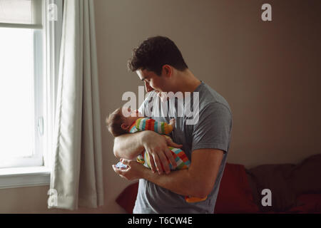 Young Caucasian père essayant de calmer bébé nouveau-né. Happy smiling mâle homme portefeuille mère enfant bascule sur ses mains. De vie authentique documen Banque D'Images