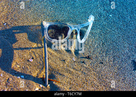 Une vieille paire de plastique blanc et transparent abandonnés lunettes laissés seuls sur la plage de sable. objets brisés et la pollution de l'air. Le plastique pollue e Banque D'Images