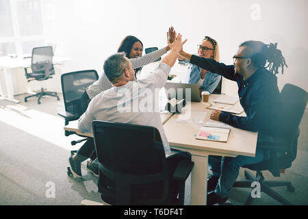 Groupe diversifié de collègues de travail de rire et de plafonnement des uns aux autres au cours d'une réunion autour d'une table dans un bureau moderne et lumineux Banque D'Images