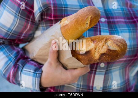 Close up of personne tenant deux baguettes fraîchement cuits dans sac en papier brun. Banque D'Images