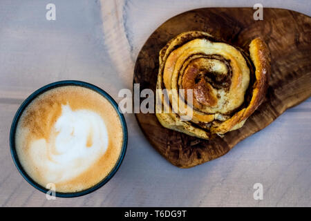 High angle portrait d'un petit pain à la cannelle fraîchement cuits au four et une tasse de Cappuccino. Banque D'Images