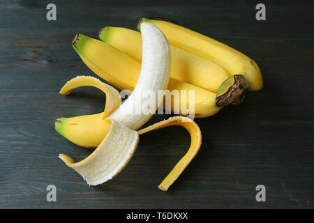 Banane pelées sur un régime de bananes isolé sur fond de bois de couleur sombre Banque D'Images