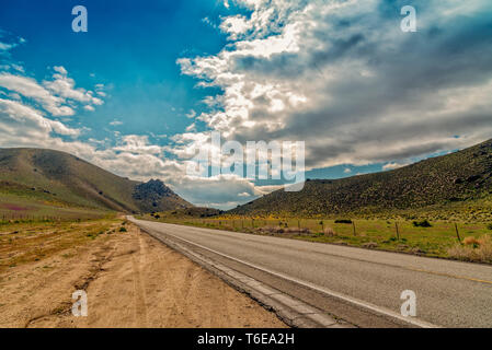 Tirez sur la route à la route de comté en montagnes sous ciel bleu avec des nuages blancs moelleux. Banque D'Images