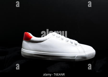 Sneakers blanc élégant avec un dos rouge sur fond sombre Banque D'Images
