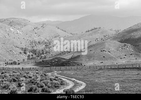 Le noir et blanc, la saleté route tournant à travers champs et pâturages en direction de collines au-delà. Banque D'Images