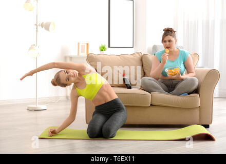 Jeune femme faire de l'exercice sur tapis, tandis que son ami stout eating chips à la maison Banque D'Images