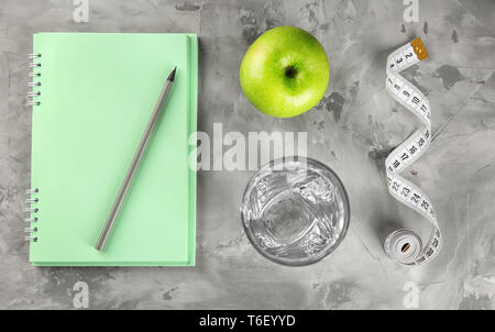 Télévision jeter la composition avec apple, verre d'eau, bloc-notes et un ruban à mesurer sur fond gris. Alimentation nourriture Banque D'Images