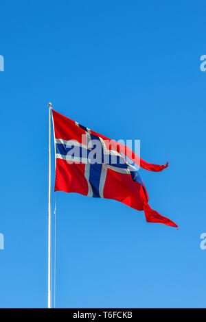 Brandir le drapeau norvégien dans le vent contre un ciel bleu Banque D'Images