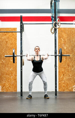 Jeune femme Body builder ou athlète faisant un squat dans une salle de sport avant la sensibilisation à ses épaules haltères en position verticale pour renforcer ses muscles Banque D'Images