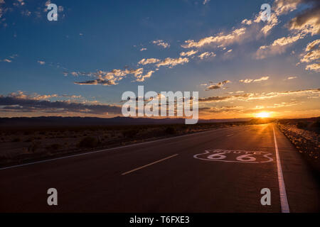 Signe de la chaussée de la route 66 à l'avant-plan et la diminution de l'angle de la route menant à un coucher de soleil spectaculaire dans le désert de Mojave, en dehors d'Ambo Banque D'Images