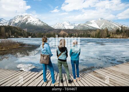 Vue arrière sur trois touristes séjournant en montagnes lac gelé - printemps entrée en Hautes Tatras en Slovaquie. Banque D'Images