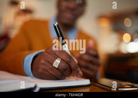Close up of contemporary African man holding pen en travaillant assis à table dans un café, copy space Banque D'Images