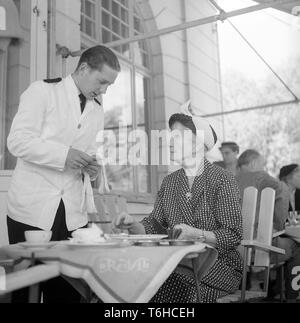 Années 50, restaurant. Une dame âgée est d'avoir une conversation avec le serveur lors du règlement de la loi. La Suède. Kristoffersson Photo BX30-6. Suède 1956 Banque D'Images