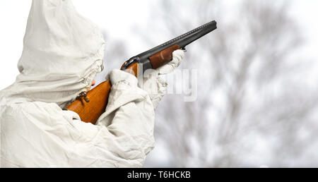 Hunter en camouflage blanc vise un fusil de chasse dans le domaine d'hiver Banque D'Images