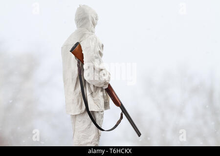 Hunter en blanc camouflage avec fusil de chasse est dans le champ d'hiver Banque D'Images