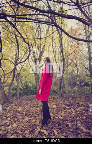 Femme au manteau rouge debout dans une clairière dans la forêt et à la tour Banque D'Images