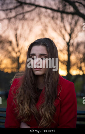 Une jeune femme assise sur un banc dans un parc, avec beaucoup sur son esprit, sentiment d'isolement et d'anxiété. Banque D'Images