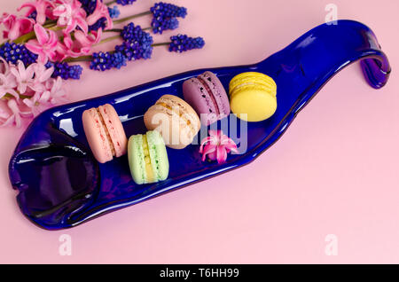 Macarons colorés sur une assiette bleue sur fond rose pastel décorées de muscari et jacinthes fleurs. Vue d'en haut. Concept dessert romantique. Spa Banque D'Images