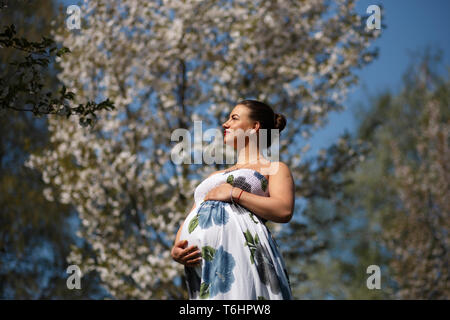 Les jeunes heureux d'être bientôt maman mère - jeune voyageur femme enceinte bénéficie de ses loisirs Temps libre dans un parc avec sakura en fleurs de cerisiers portant un Banque D'Images