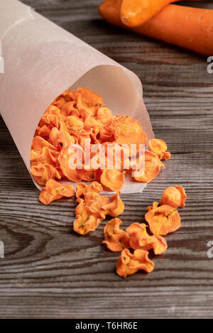 Chips de carotte orange tombant de sac en papier blanc à la vieille table en bois. Banque D'Images