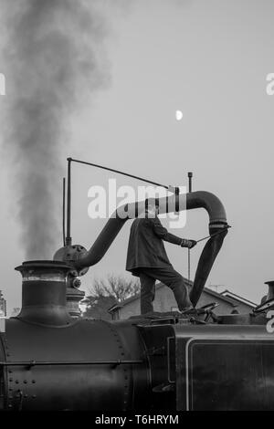 Tourné en noir et blanc de membre d'équipage de la locomotive à vapeur isolés au sommet d'vintage UK machine à vapeur à l'aide d'une grue et de l'eau remplir le réservoir d'eau. Banque D'Images