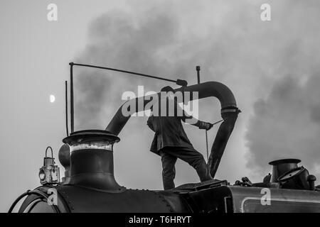 Tourné en noir et blanc de membre d'équipage de la locomotive à vapeur isolés au sommet d'vintage UK machine à vapeur à l'aide d'une grue et de l'eau remplir le réservoir d'eau. Banque D'Images