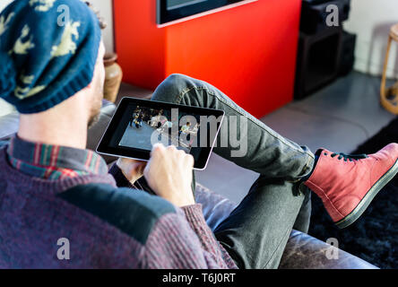 Un jeune homme assis sur le canapé à la maison tout en relaxant à l'aide d'une tablette. Banque D'Images