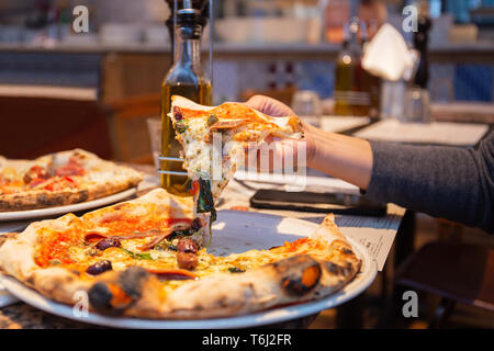 La prise de main de tranches de pizza savoureuse de la plaque en restaurant. Banque D'Images