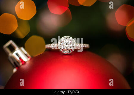 Bague de fiançailles sur un ornement de Noël avec des lumières à l'arrière-plan. Banque D'Images