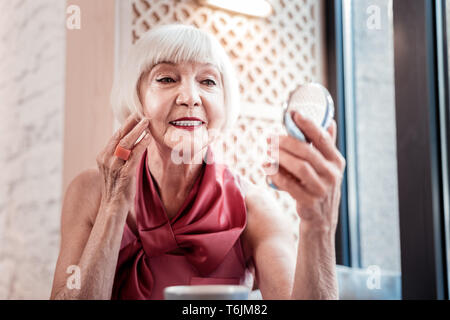 Femme aux cheveux gris et souriant avec Bob coupe de l'examen de son maquillage Banque D'Images