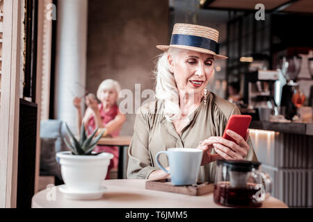 À Poil long attrayante Vieille Femme au chapeau de paille en observant son smartphone Banque D'Images