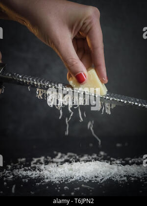 Mains d'une femme de parmesan râper sur fond noir. Dark de la nourriture. Fromage Parmigiano Reggiano italien Banque D'Images